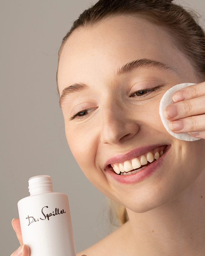 Woman cleanses face with cotton pad and tonic