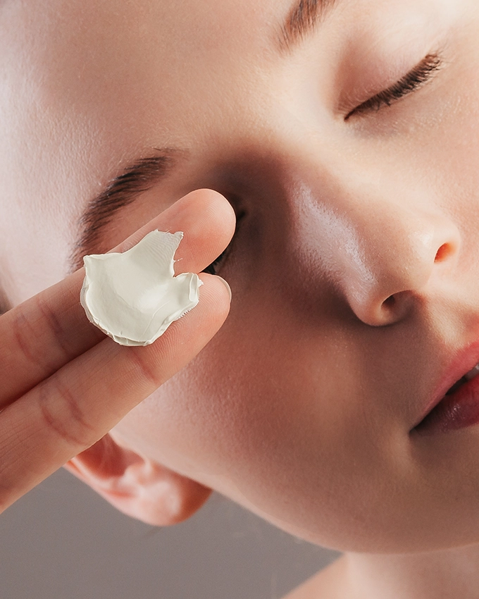 Creme auf zwei Fingern wird vor Gesicht von Frau gehalten