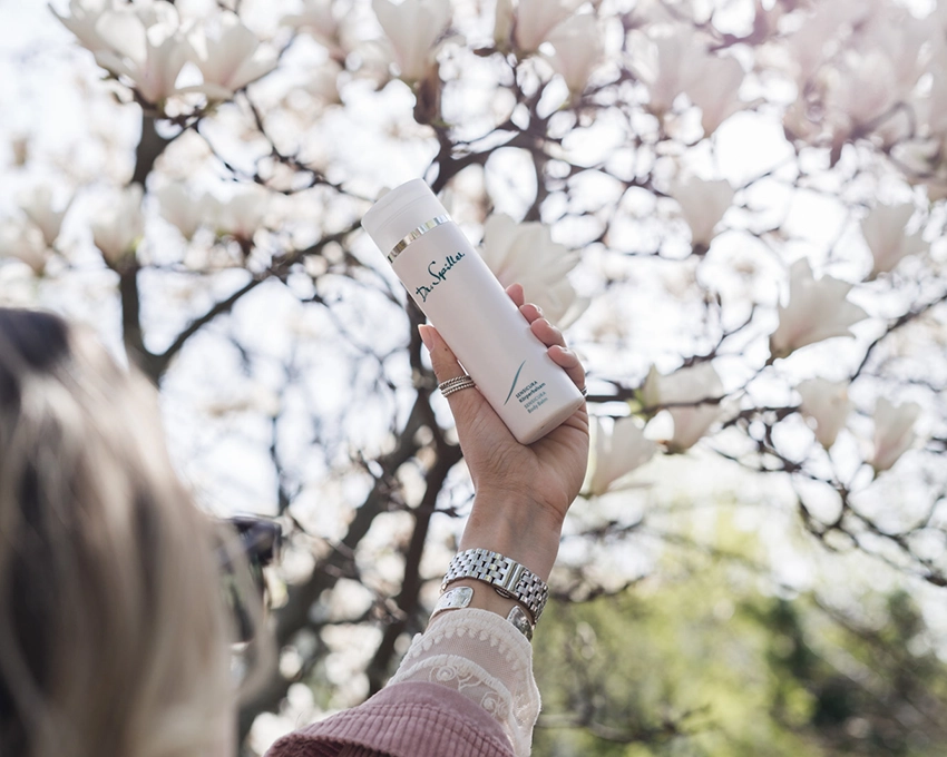 Sensicura body balm is held in the air in front of a magnolia tree
