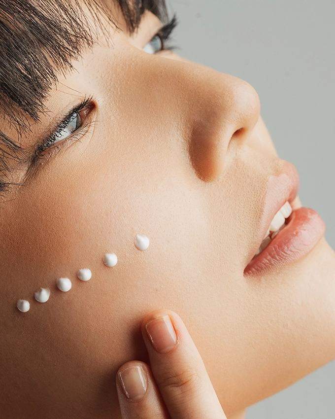 Serum wird punktuell auf Wange von Frau aufgetragen