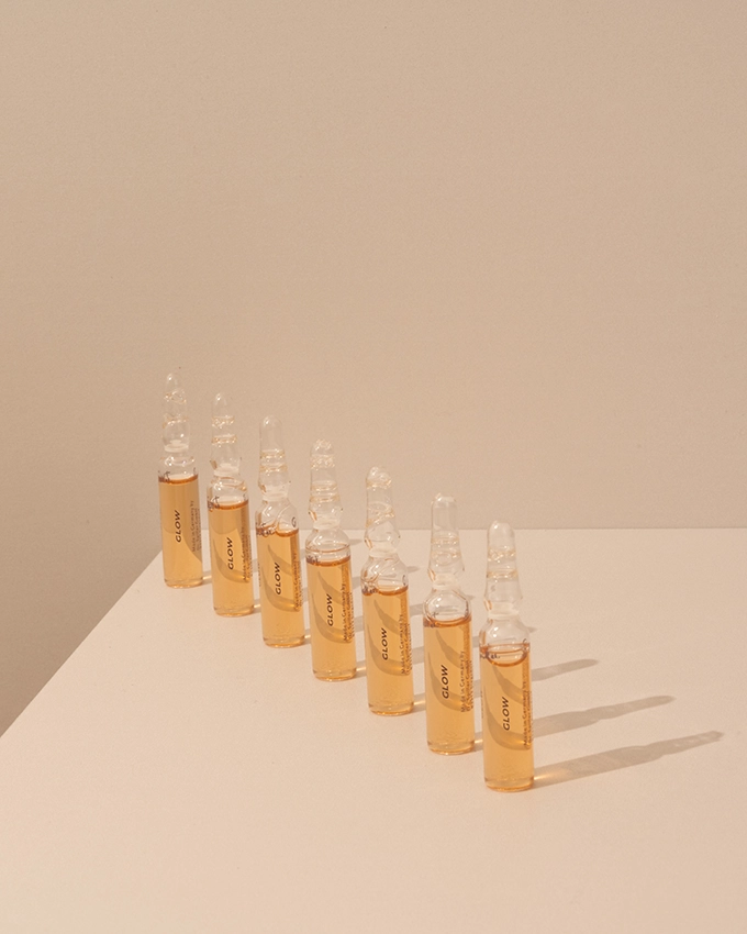 Several ampoules are placed on a table with a pink background