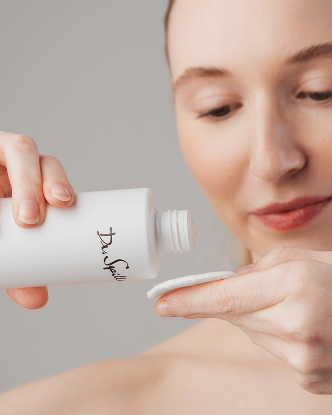 Woman cleanses face with cotton pad and tonic